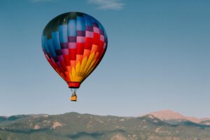 Vibrant hot air balloon soaring over the majestic mountains of Colorado Springs during daylight.